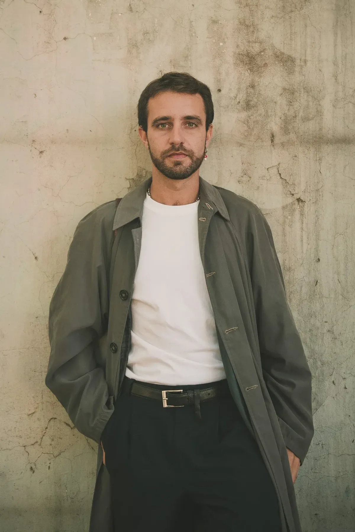 Juna leaning on a concrete wall, white tee and grey overcoat