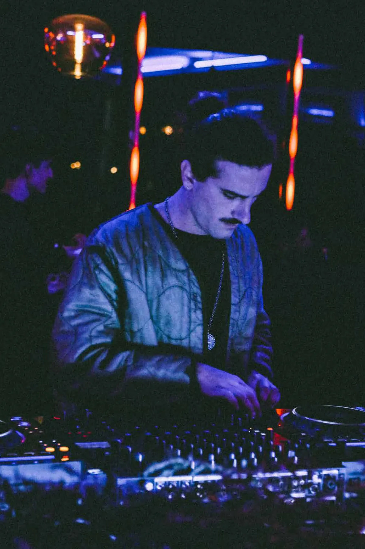 Ocho in the DJ booth under blue lights, disco ball above